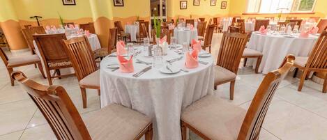 Un comedor con mesas redondas, sillas de madera y manteles blancos.