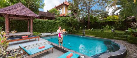 A swimming pool with lounge chairs and a gazebo, surrounded by lush greenery and a house in the background.