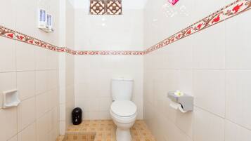 Un baño pequeño con azulejos, que incluye un inodoro, un bote de basura, un secador de manos y un dispensador de pañuelos.