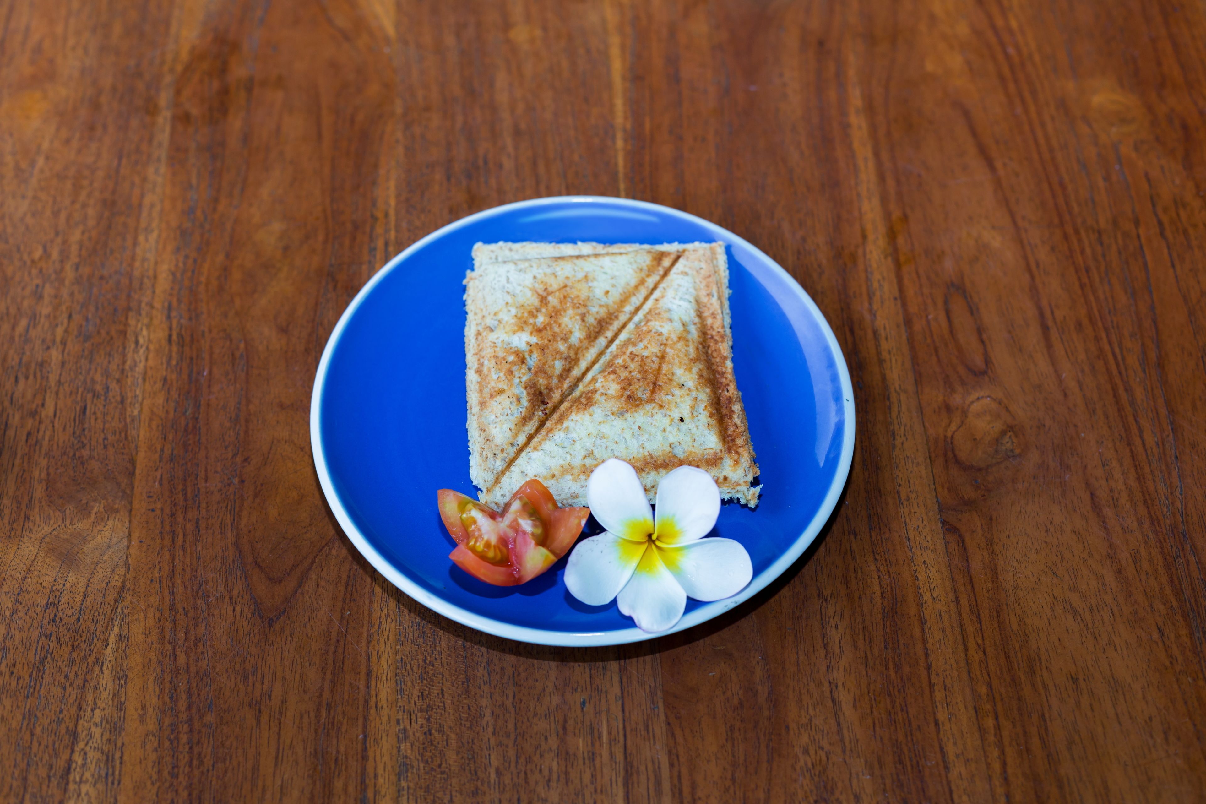 Un sándwich en un plato azul, con una flor y una rodaja de tomate.