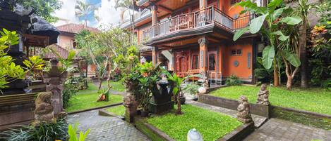 Un edificio tradicional de varios pisos con un patio que presenta estatuas de piedra, una fuente de agua y abundante vegetación.