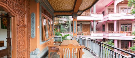 An ornately decorated room with a wooden table and chairs, a balcony with a railing, and a view of adjacent buildings.