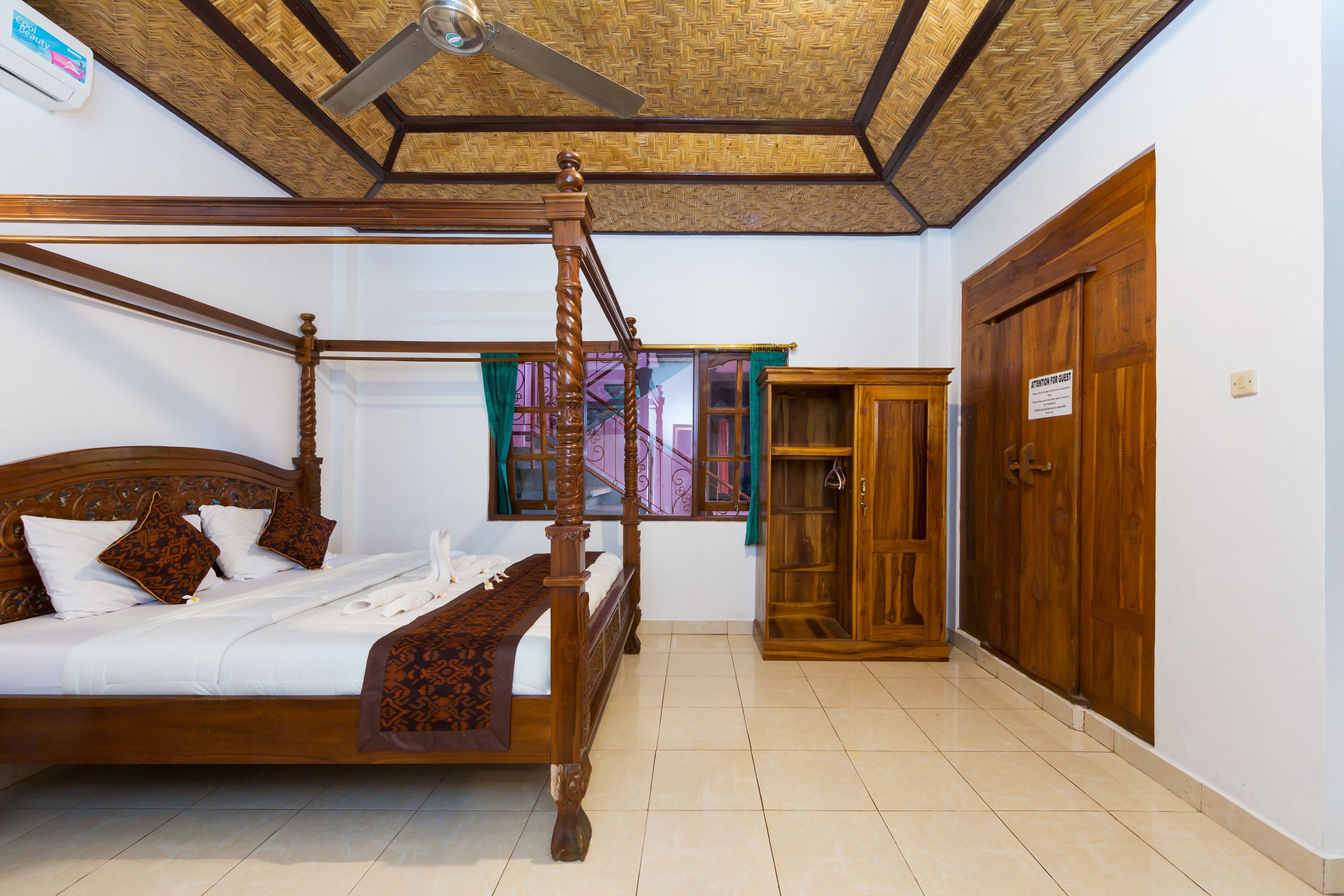 A four-poster bed with a wooden headboard, a ceiling fan, and a wooden wardrobe with a sign on the door.