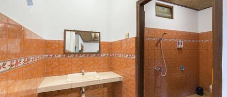A bathroom with an orange patterned wall, a sink, a mirror, and a shower area.