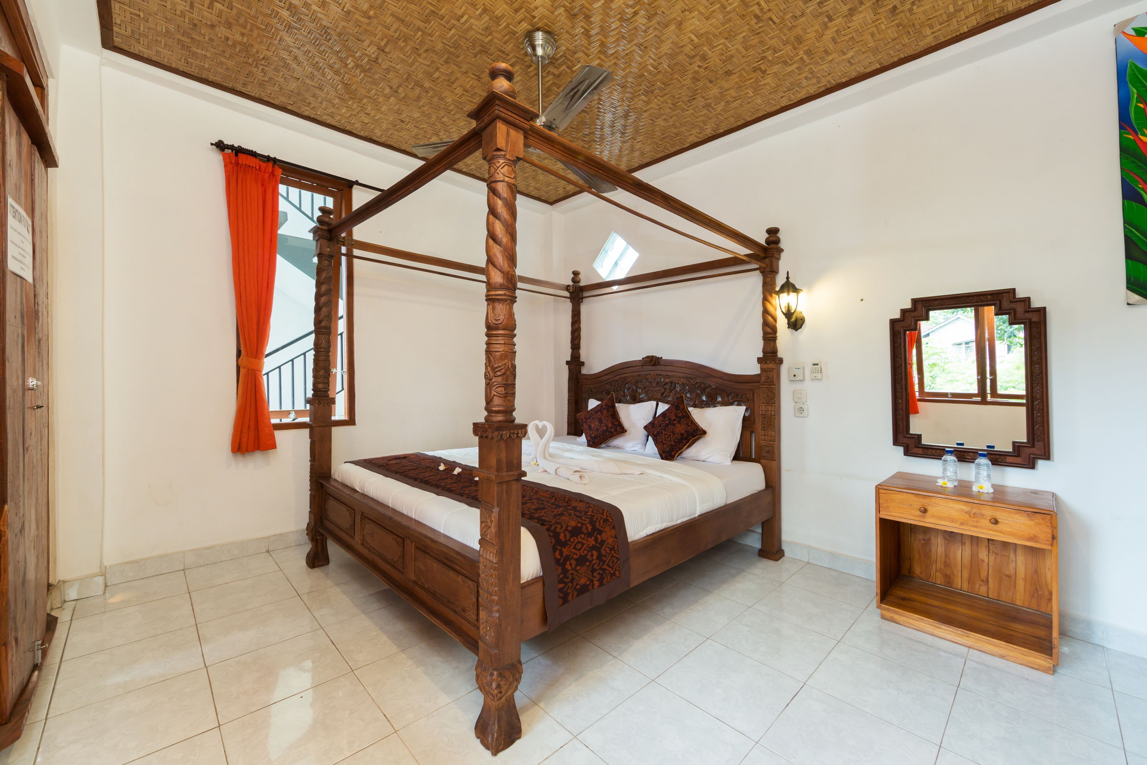 A four-poster bed with a wooden frame, a bedside table with two bottles, and a mirror on the wall.