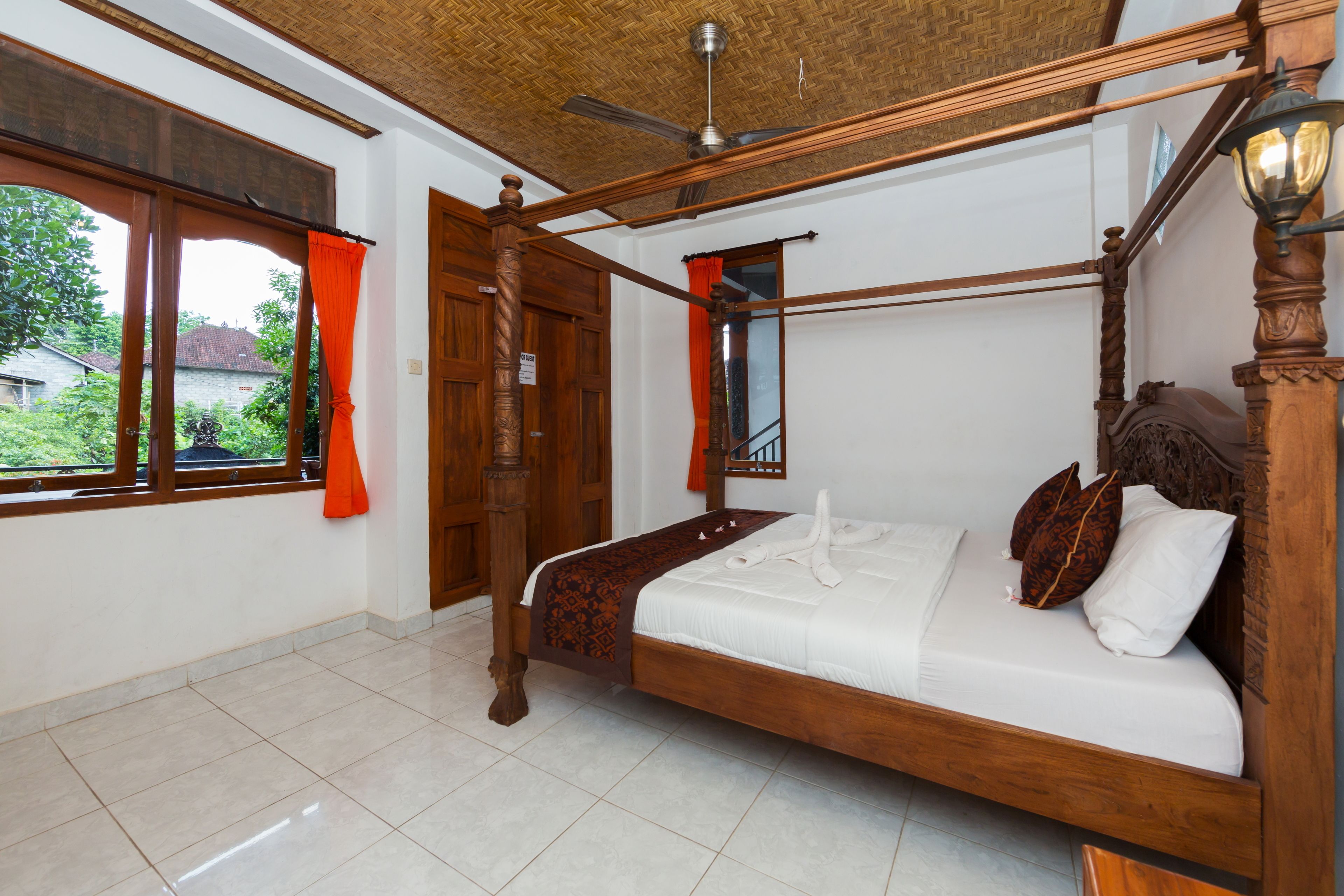 Een bed met hemelbed, met een houten frame, wit beddengoed en decoratieve kussens.
