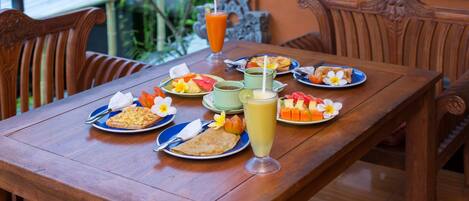 A wooden dining table with plates of food, a glass of juice, and a flower.