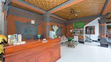 A reception area with a wooden desk, a ceiling fan, and a staircase leading to another level.