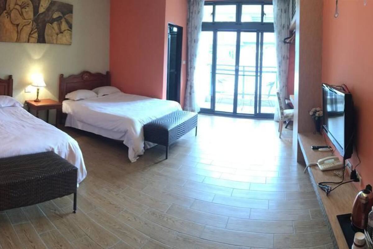 A hotel room with two beds, a TV, a desk with a lamp, and a large window.
