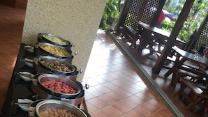 A buffet line with various dishes in metal containers, including meats and salads, in a room with tiled flooring and wooden furniture. - Lins Ju Homestay (Yuchi)