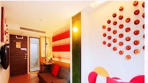 Habitación de hotel con cama, sofá, pared decorada con motivos circulares y puerta que da a otra habitación.