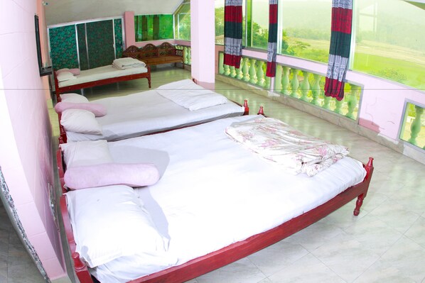 A room with three single beds, a wooden bench, and a view of a green landscape through large windows.