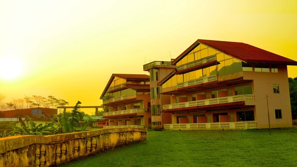 A multi-story building with balconies and a large glass facade, surrounded by greenery and a stone wall. - Jaintia Hill Resort (Gowainghat)