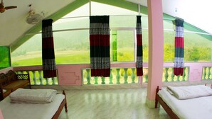 A room with two beds, a ceiling fan, and a view of a green landscape through large windows. - Jaintia Hill Resort (Gowainghat)