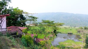 A rural landscape with a house, a pond, and a view of distant hills. - Jaintia Hill Resort (Gowainghat)