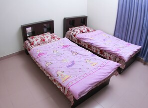 Two single beds with floral bedding, wooden headboards, and a plain wall. - Hillside Holiday Home (Sylhet)