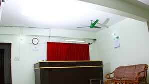 A reception area with a black counter, a red curtain, a wooden chair, and a ceiling fan. - Hillside Holiday Home (Sylhet)