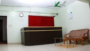 A reception area with a black counter, a red curtain, a wooden chair, and a ceiling fan.