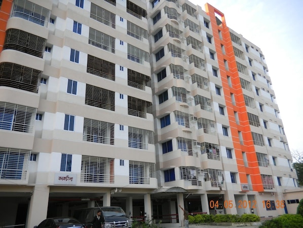 A multi-story building with balconies and a parking area.