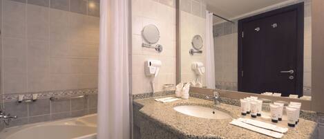 A bathroom with a bathtub, two sinks, a mirror, and toiletries on the counter.