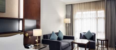 A hotel room with a bed, a sofa, a small table, a lamp, and a window with curtains.