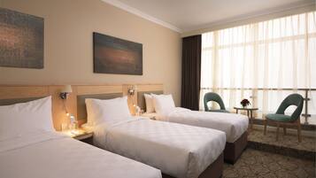 A hotel room with three beds, a small table with a flower, and a chair.
