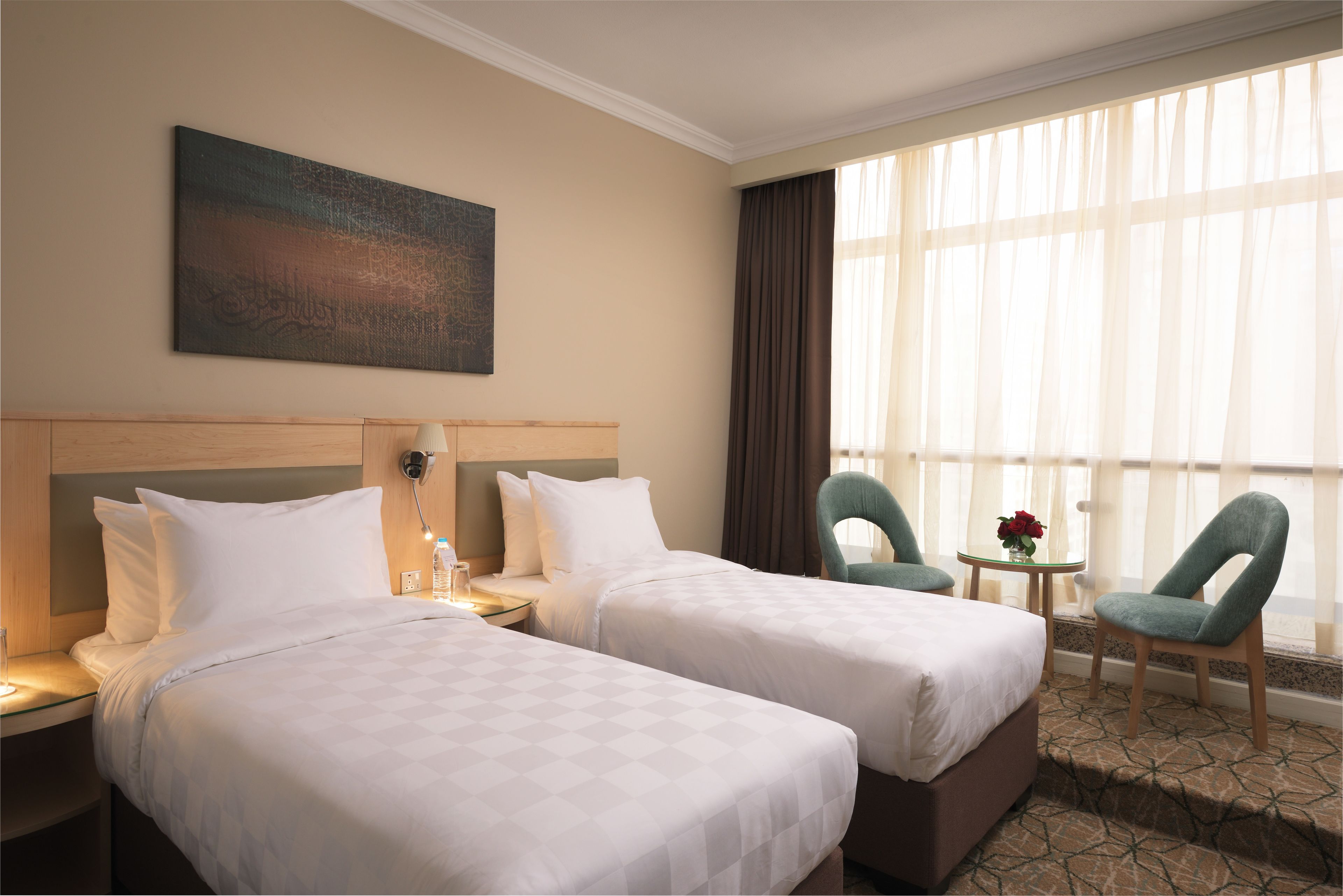 A hotel room with two beds, a nightstand, a lamp, a chair, a small table with a vase, and a large window with curtains.