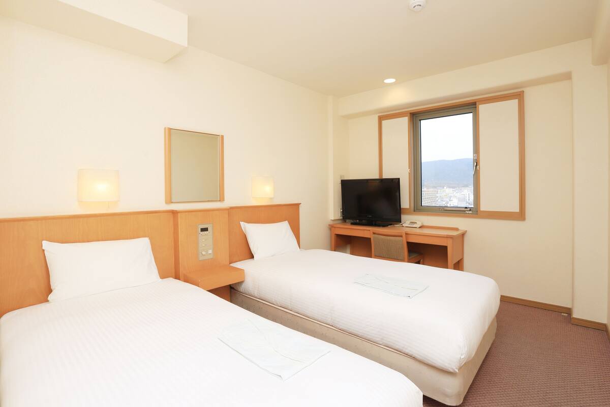 A hotel room with two beds, a television, a desk with a computer, and a window with a view.