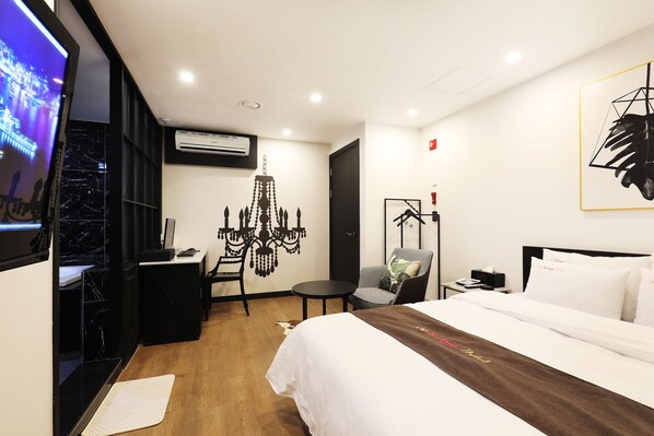 Habitación de hotel moderna con una cama grande, un escritorio, una silla, un televisor y una araña.