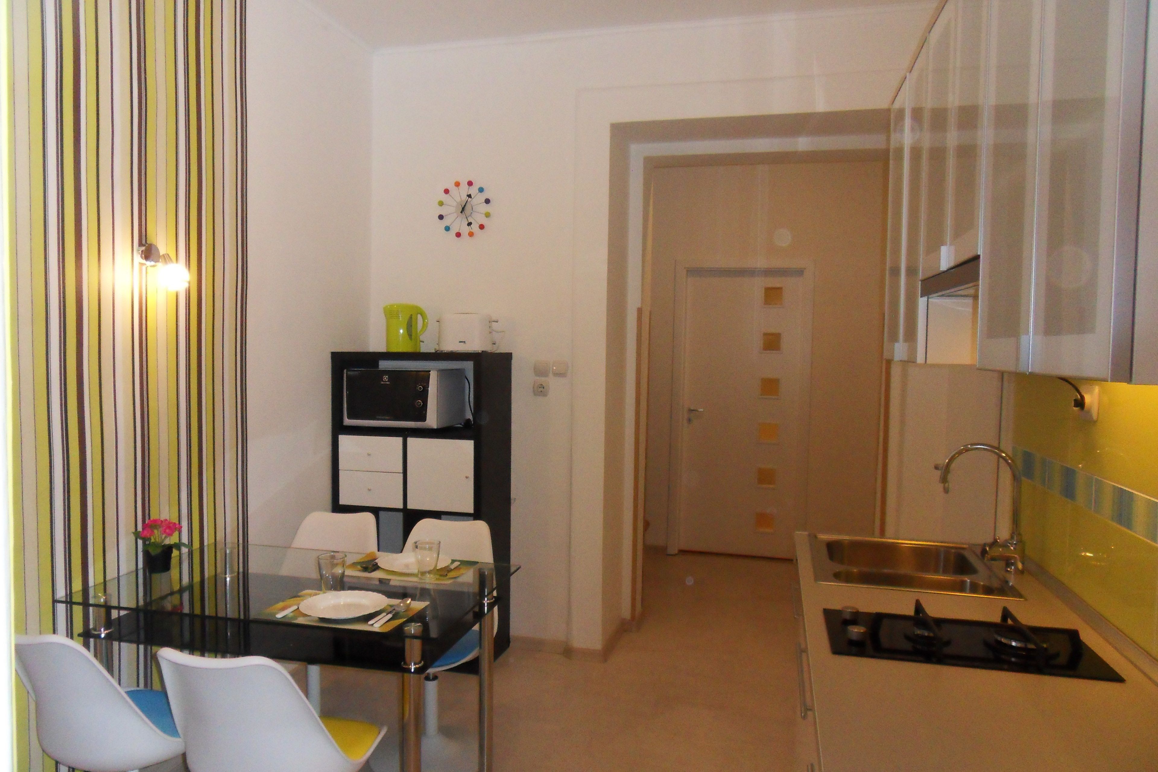 Una cocina compacta con estufa a gas, un fregadero y una zona de comedor con mesa de vidrio y sillas.