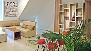 A modern living room with a sofa, coffee table, and red chairs. There is a bookshelf with decorative items and a painting on the wall. - The Alley City Hotel (Denpasar)