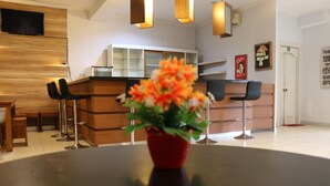 A modern kitchen with wooden cabinets, a black countertop, and a red vase with flowers on a round table. - The Alley City Hotel (Denpasar)