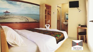 A hotel room with a bed, a painting of a beach, a wooden wardrobe, a desk with a chair, and a TV mounted on the wall. - The Alley City Hotel (Denpasar)