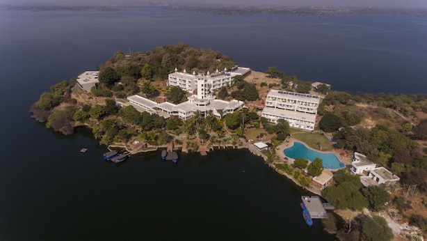 Vue aérienne d’un vaste complexe hôtelier de luxe situé sur une île, avec de nombreux bâtiments, une piscine et des bateaux amarrés.
