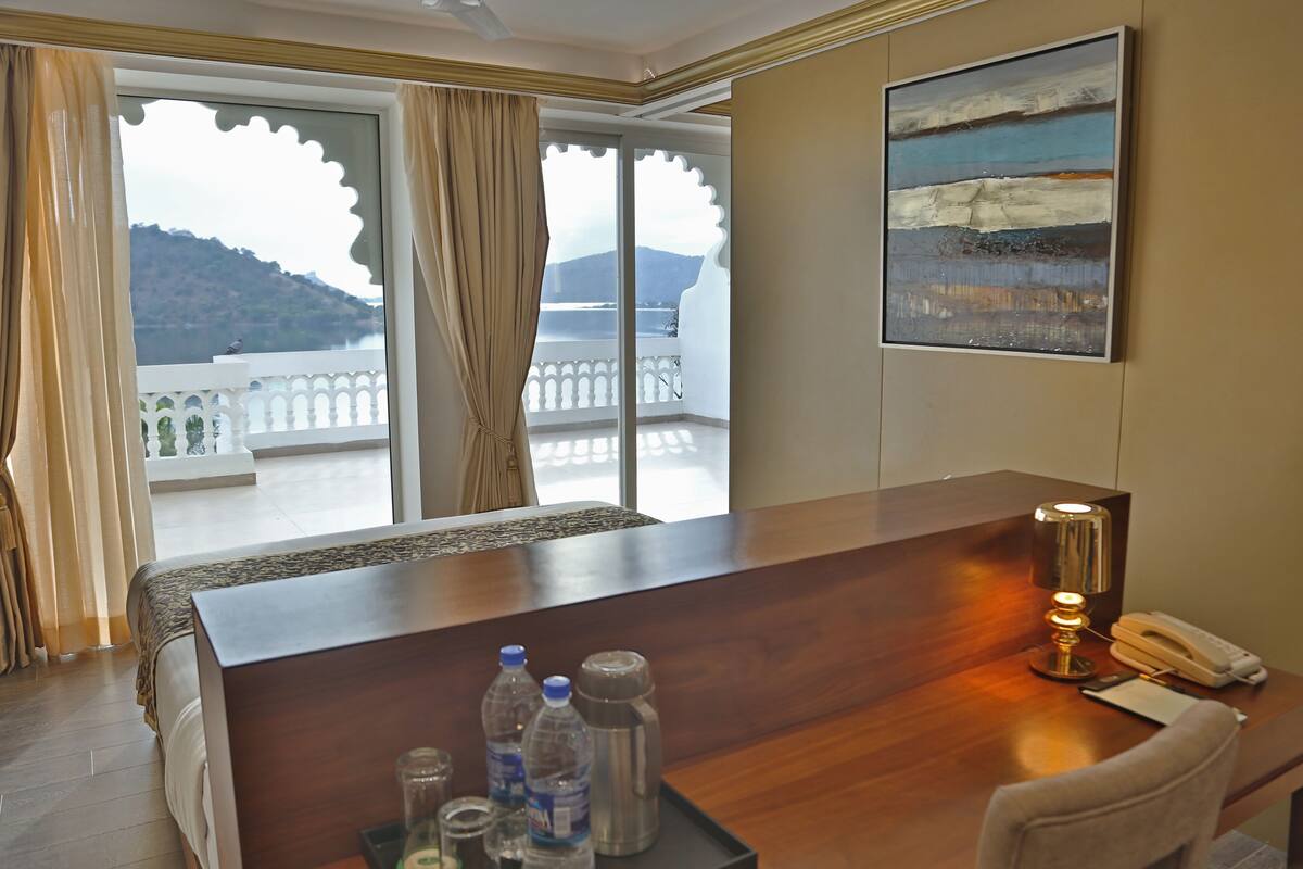 Ein Hotelzimmer mit einem Holztisch, einem Telefon, einer Lampe und Blick auf einen Balkon mit einem Berg im Hintergrund.