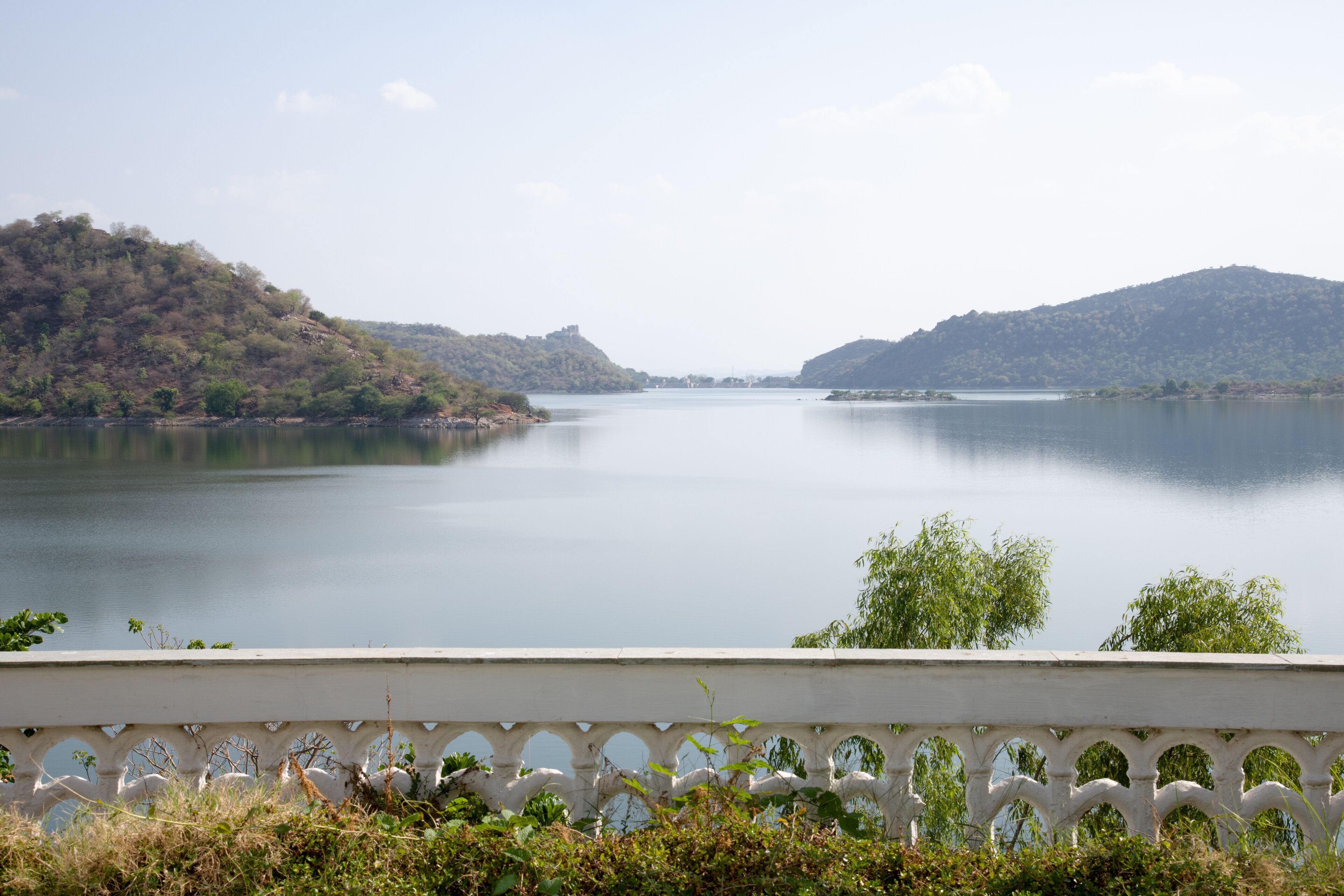 Un lago tranquilo con colinas al fondo y una cerca blanca en primer plano.