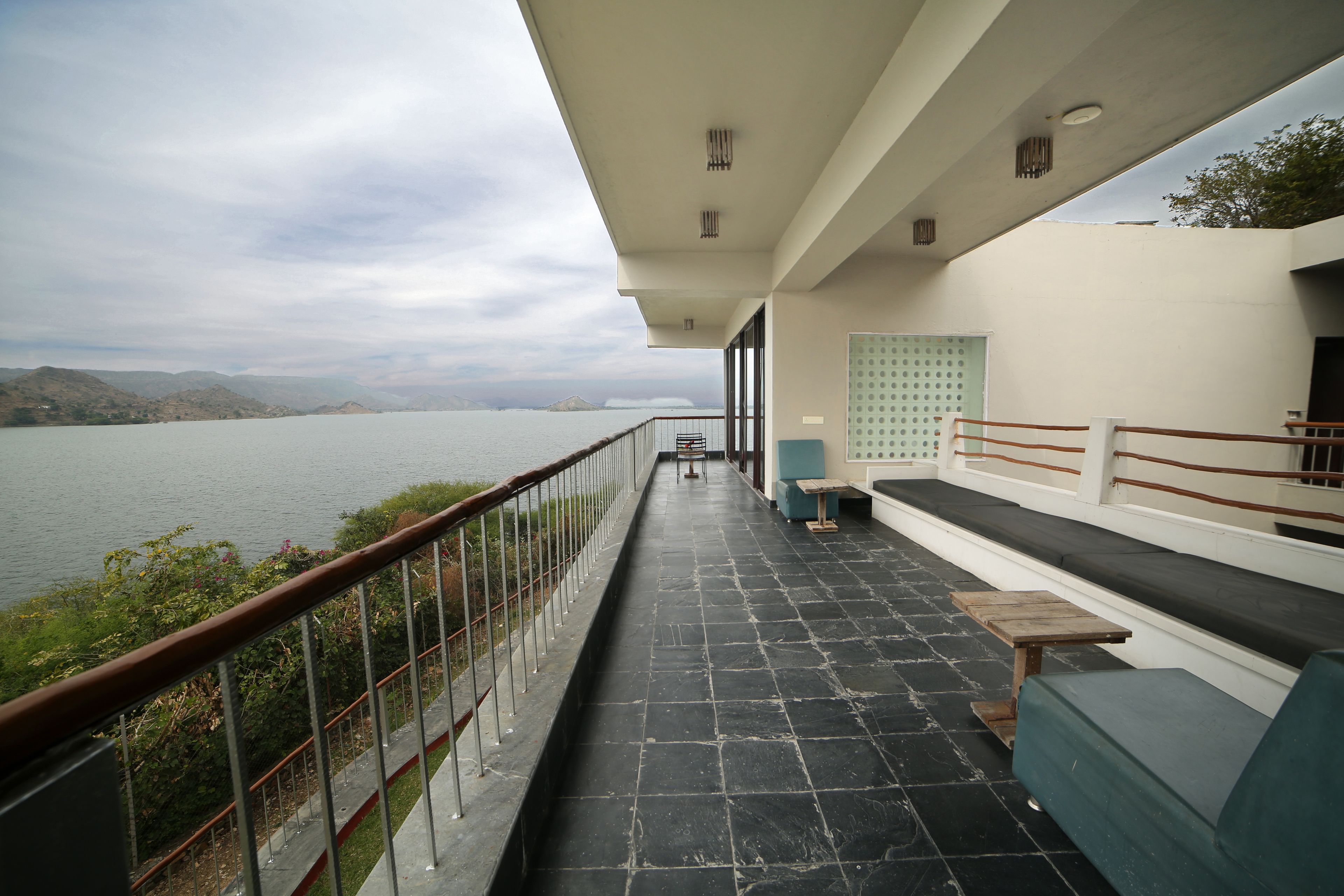 Un balcón con vista a un lago, una zona de estar con un sofá y una mesa, y una barandilla en el borde.