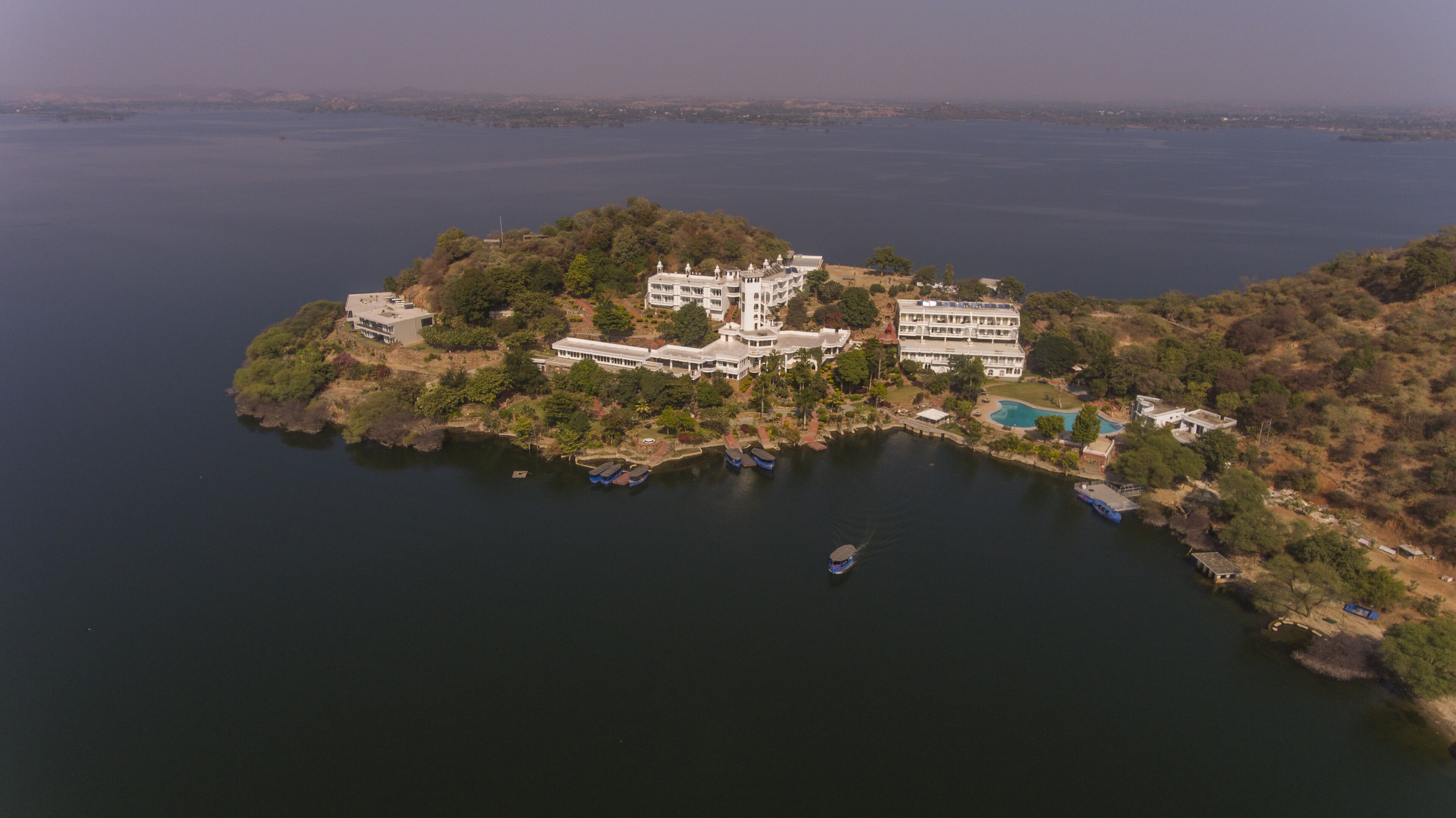 An aerial view of a large, multi-story resort with a pool and several boats on the water.