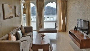Un salon moderne avec un canapé, une table à manger et un téléviseur. Il y a un balcon avec des rideaux et une vue sur une montagne.