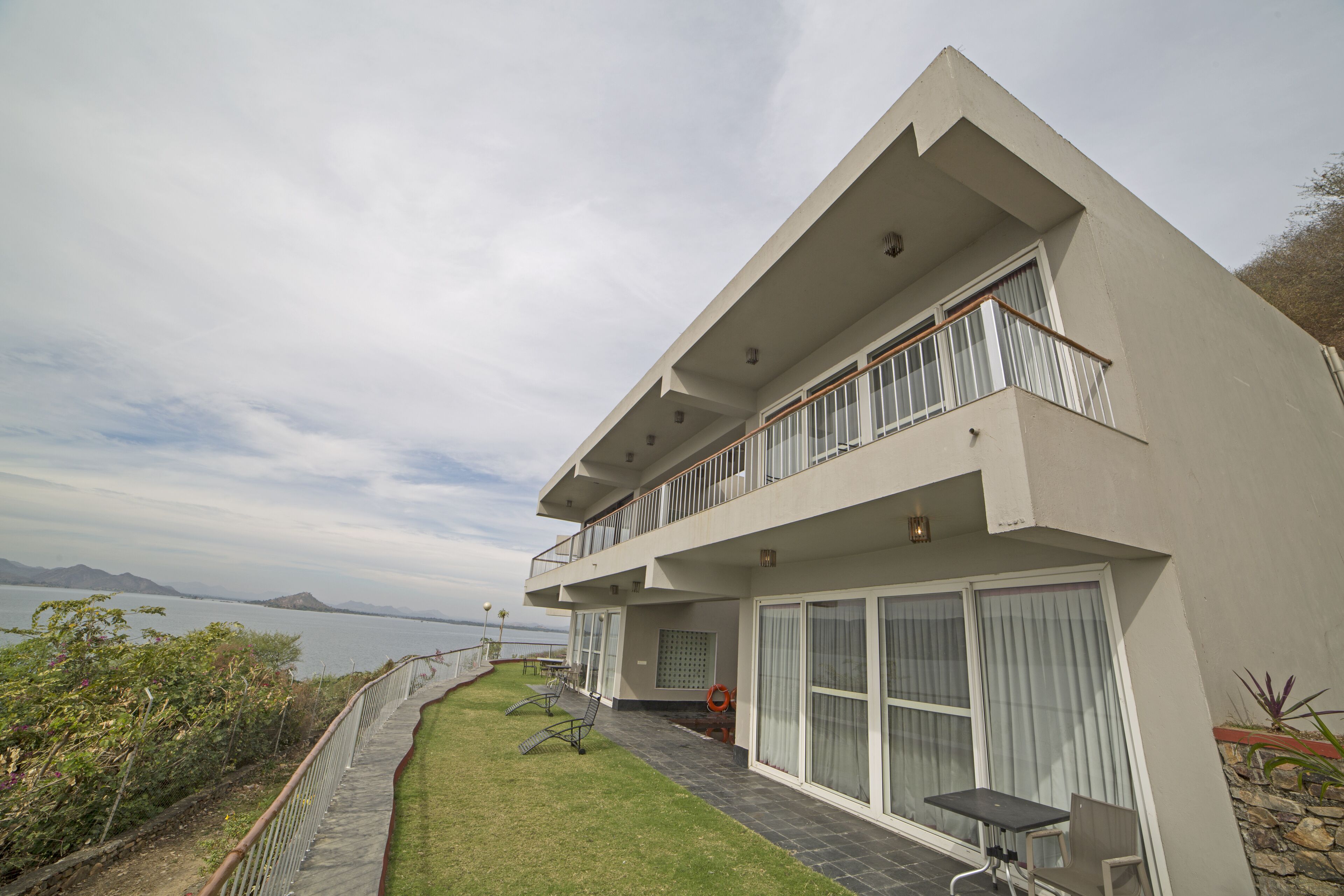 A modern two-story building with a balcony, large windows, and a view of the sea.