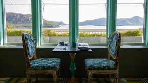 Un coin repas avec deux chaises et une table, une vue sur un plan d’eau et des collines, et une fenêtre ornée d’un cadre décoratif.