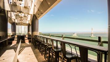 Un restaurante con vista a un puente sobre el agua, que cuenta con una barra larga con sillas y lámparas colgantes.