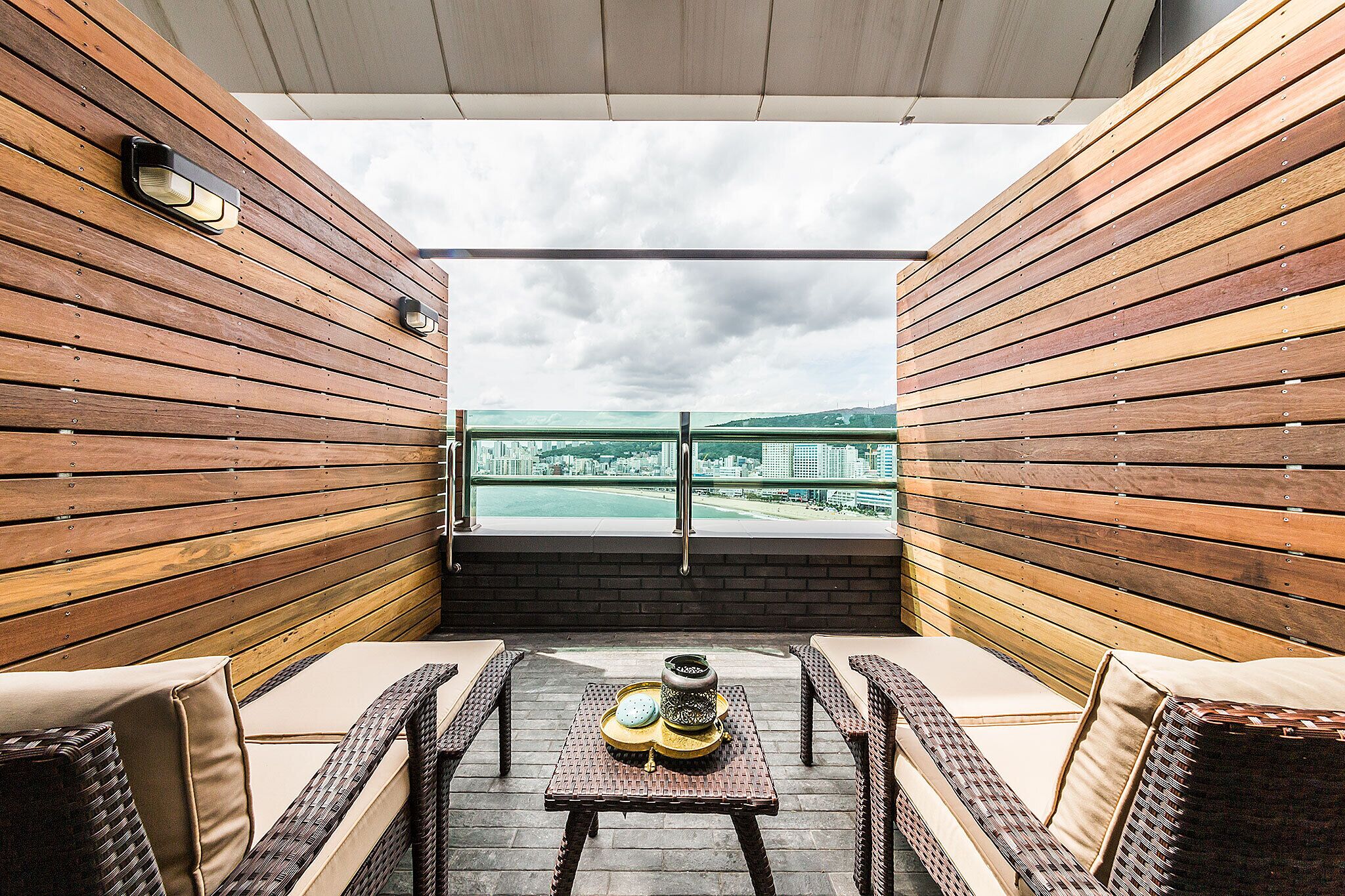 Un balcón con paneles de madera, una mesa con una bandeja de objetos y vistas a un paisaje urbano.