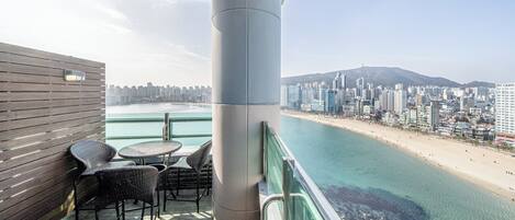 A balcony with wicker chairs and a table overlooking a beach and cityscape.