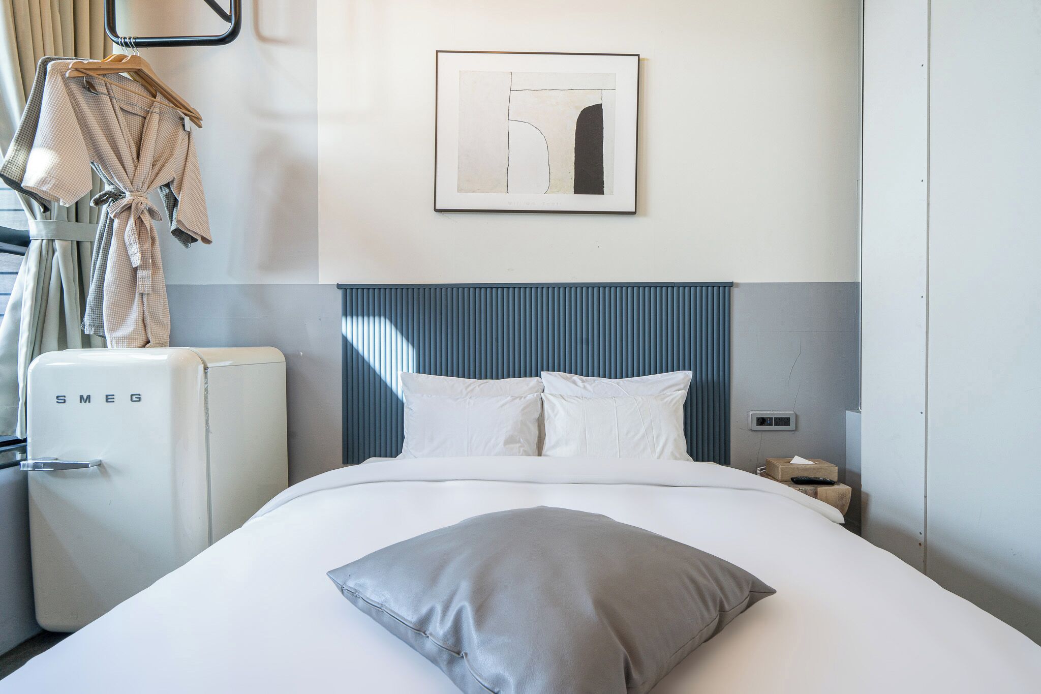 Una camera d'albergo con un letto, un frigorifero bianco, un portascopevoli e un quadro appeso al muro.