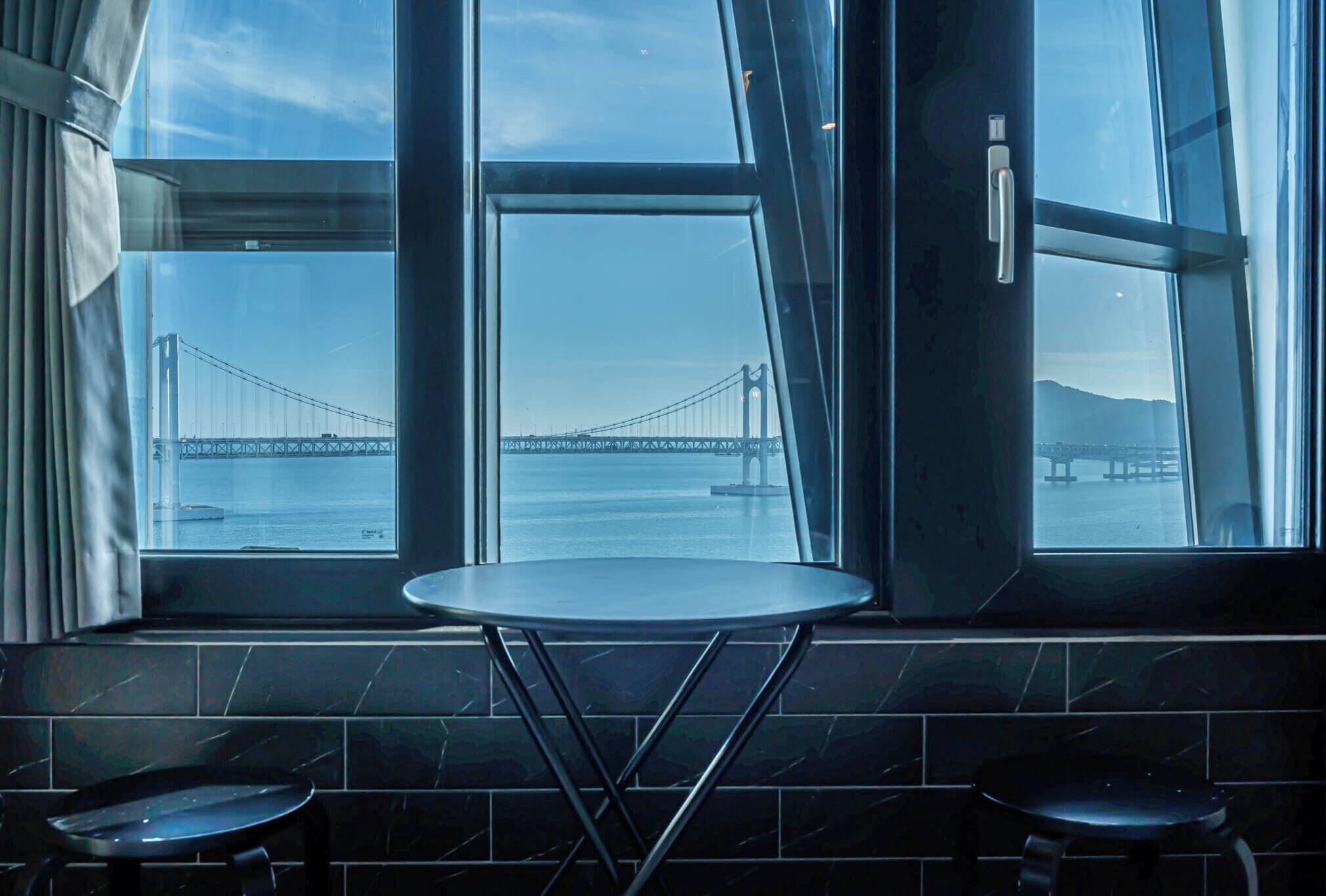 Habitación con un ventanal grande que da a un puente. Hay una mesa redonda pequeña y dos taburetes.