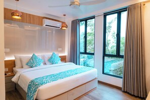 Una habitación de hotel moderna con una cama grande, un ventilador de techo, un equipo de aire acondicionado, una ventana con cortinas y vistas a zonas verdes.
