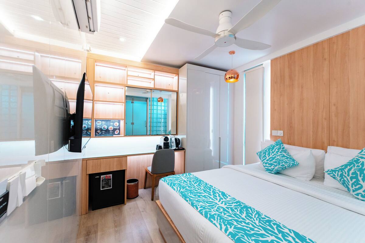 A hotel room with a bed, a desk with a chair, a wardrobe, and a ceiling fan.