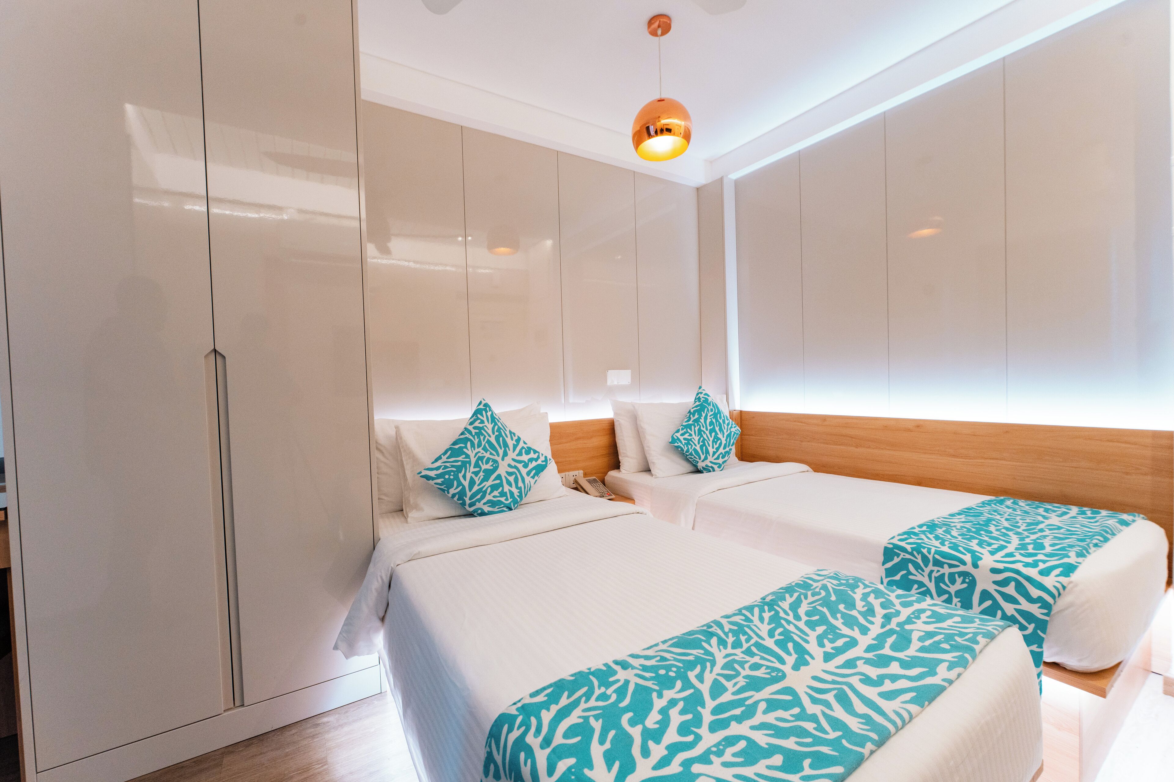 A hotel room with two beds, a wardrobe, and a hanging light fixture.