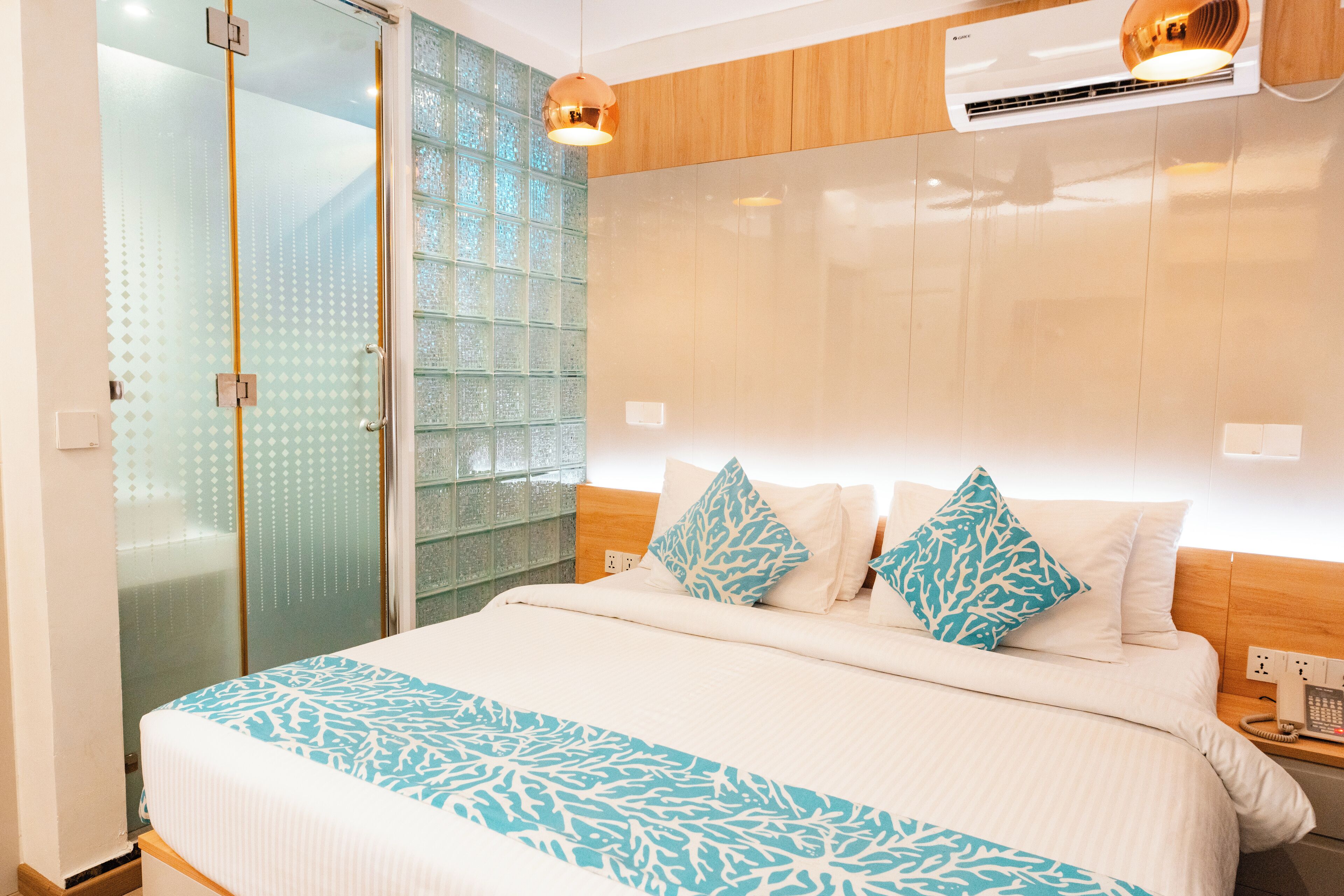 Quarto de hotel moderno com uma cama grande, box de vidro e cabeceira de madeira.